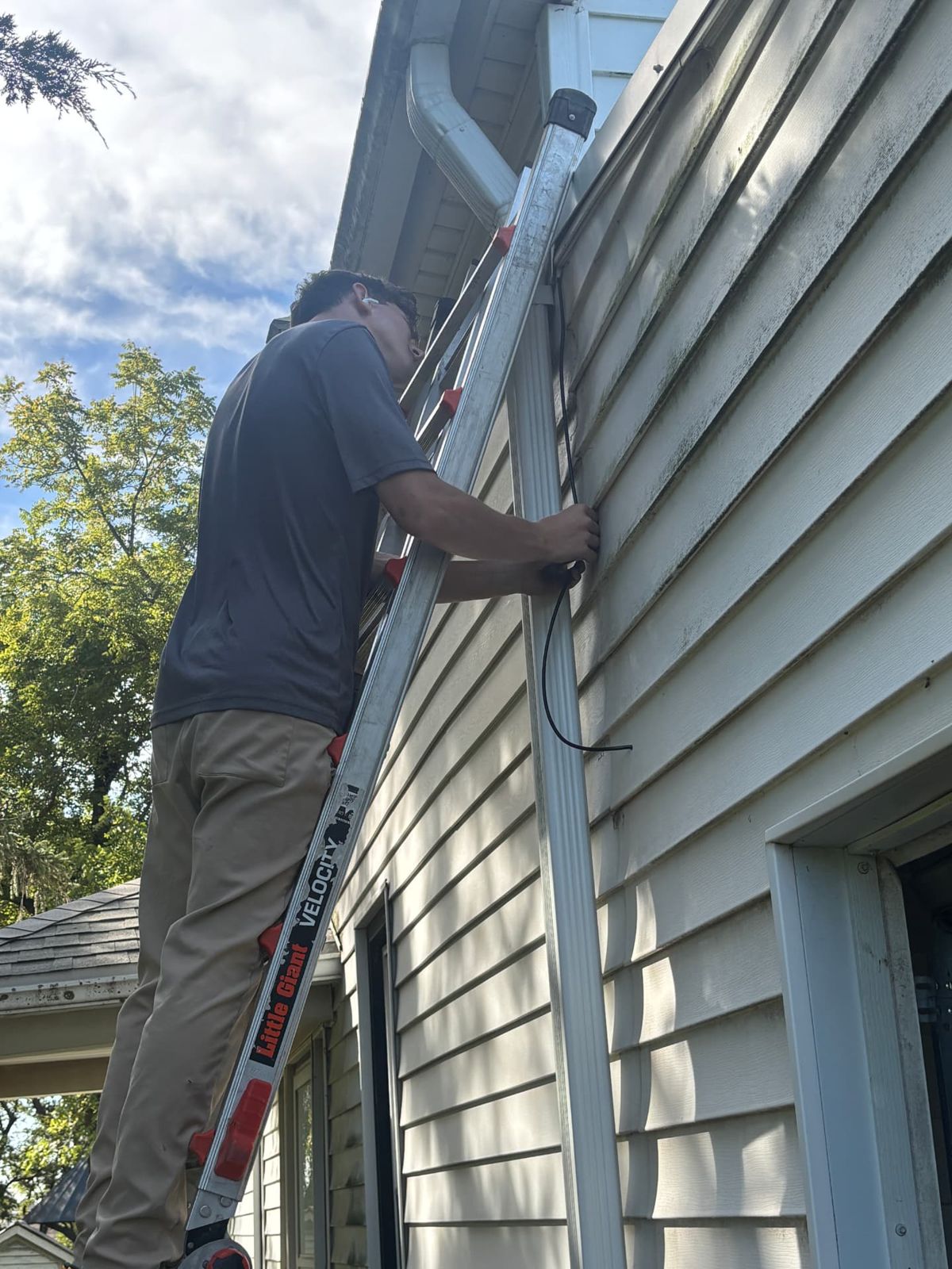 All Things Tech technician on a ladder routing security camera cable along the eave of a home