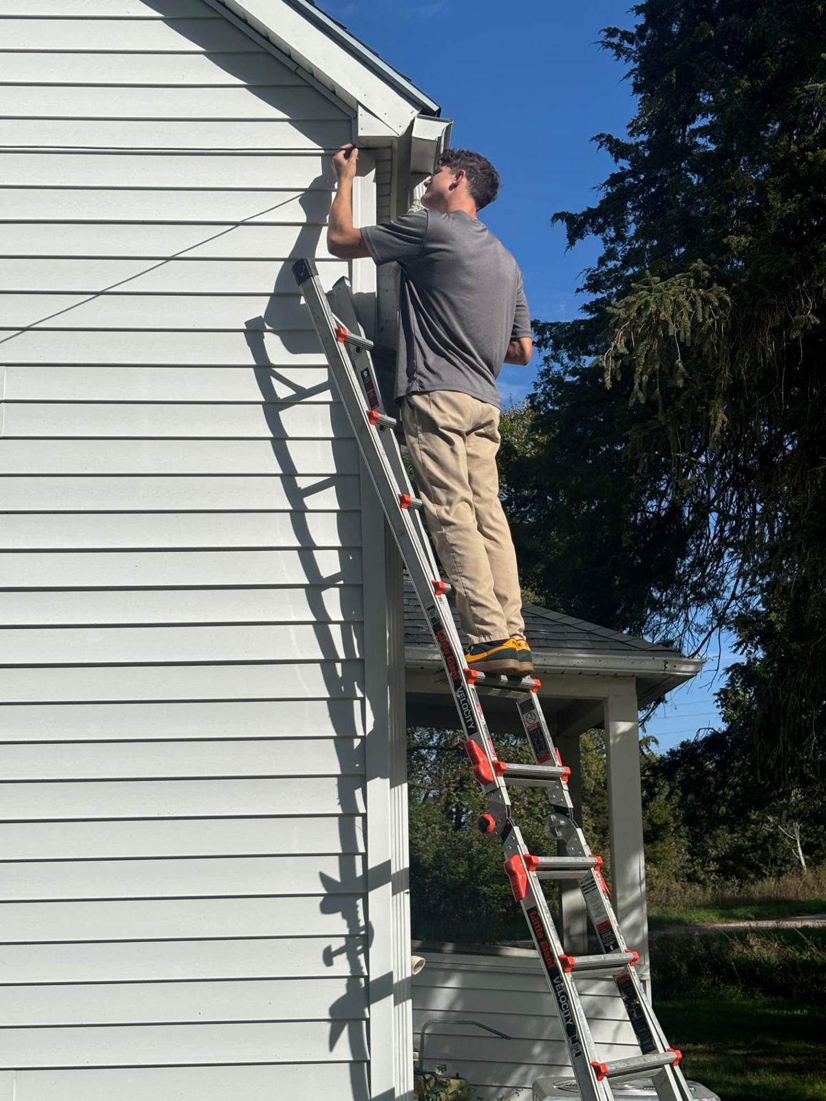 Technician running outdoor camera cable along the gable trim of a house