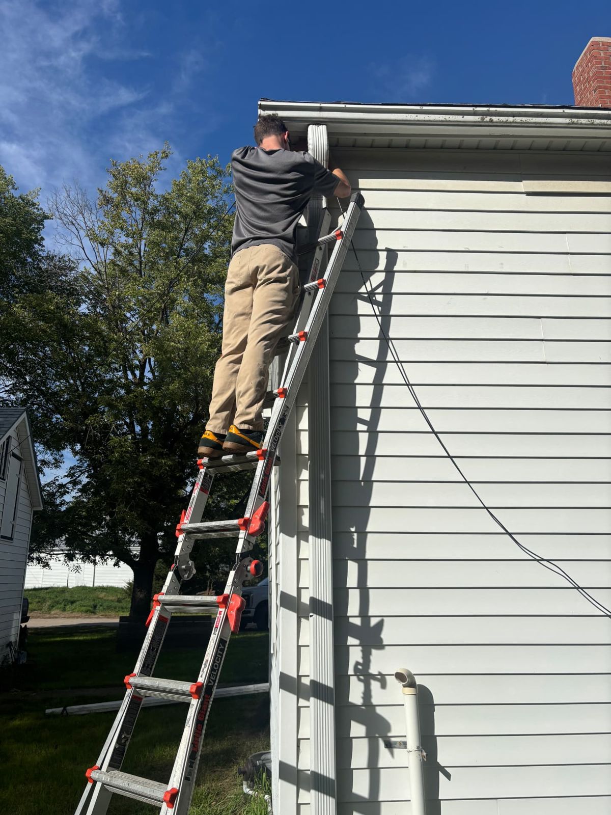 Technician routing security camera cable at the corner of a house near the gutter