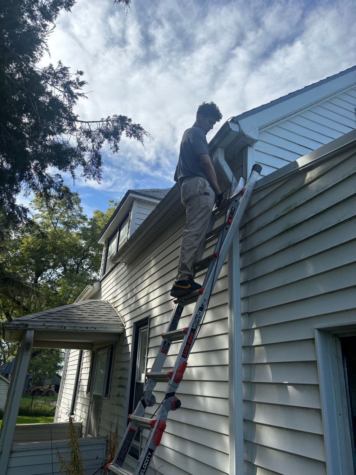 All Things Tech technician on a ladder working at the roofline of a rural home during a camera installation